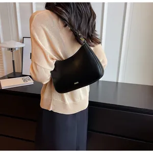 Close-up of black matte hobo bag with gold metal logo on a model in beige knitwear