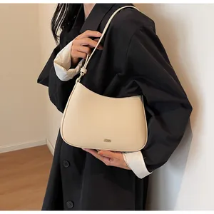 Detail of minimalist cream leather half-moon shoulder bag with sleek metal logo and stitching