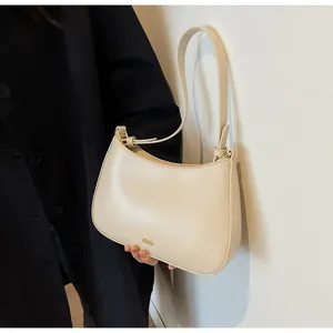 Detail view of smooth cream leather underarm bag with golden logo and fine stitching