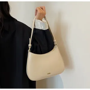 Close-up of minimalist beige faux leather shoulder bag with gold metal logo and chain