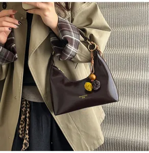Detail van donkerbruine hobo-tas met glanzende afwerking en pluche hanger bij een model