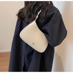 Close-up of minimalist cream underarm bag with smooth curved design and metal logo detail