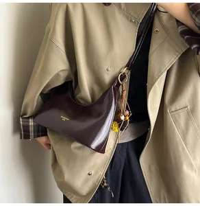 Detail van een donkerbruine glanzende leren hobo tas met goudbeslag en kralenkwastje