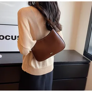Detail of a dark brown half-moon underarm bag featuring a metallic logo and sleek finish