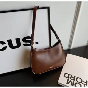 Detail of a brown leather crescent shoulder bag with gold hardware and logo