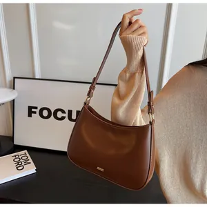Detail of brown leather crescent underarm bag with gold logo and adjustable shoulder strap
