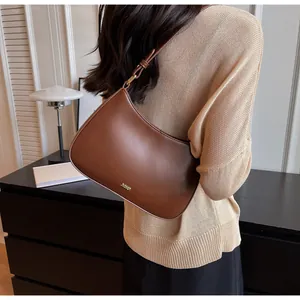 Detail view of the brown leather underarm bag with gold logo on a beige knit sweater