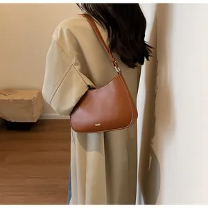 Detail view of brown leather crescent bag with golden brand logo and metallic hardware
