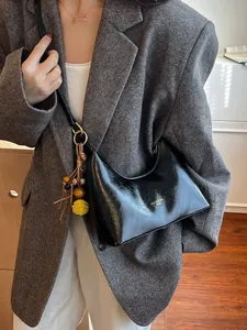 Glanzende zwarte hobo schoudertas van kunstleer met decoratieve kwast en goudkleurig logo