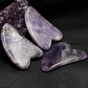 Drei herzförmige Amethyst-Gua-Sha-Massagewerkzeuge auf einem schwarzen strukturierten Hintergrund