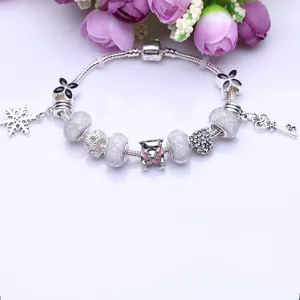 Armband im Pandora-Stil mit silbernen Anhängern und matten Perlen auf weißem Blumenhintergrund