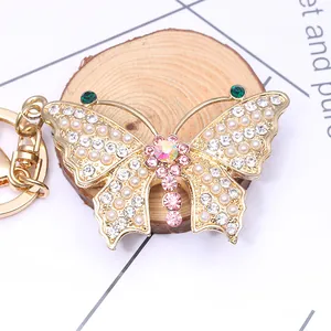 Golden butterfly keychain with pearls and crystals on a rustic wooden base display
