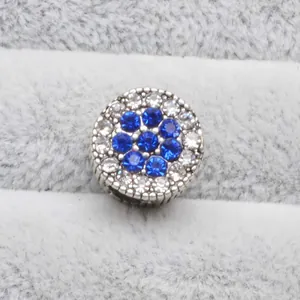 Vue macro d'un charm argenté avec motif floral en strass bleus et détails blancs