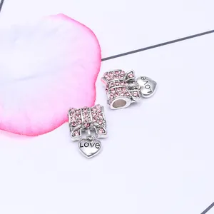Détail de breloque nœud argenté avec cristaux roses et pendentif cœur gravé Love