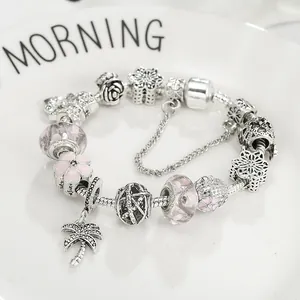Pulsera con abalorios rosa y colgante de palmera plateada sobre cerámica blanca