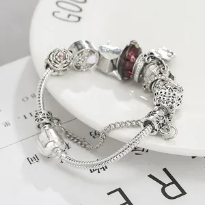 Versilbertes Schlangenarmband mit rosa Rosen und Herzanhängern in einer weißen Schale