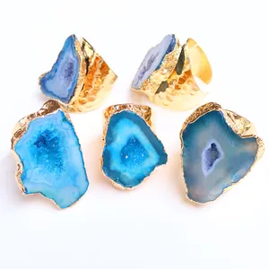 Dettaglio di cinque anelli in geode di agata blu grezza con fasce in metallo martellato oro