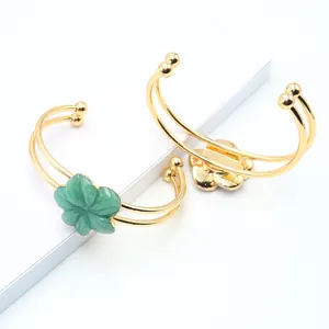 Dual gold-tone open bangles with green quartz flower charms and elegant metal finish