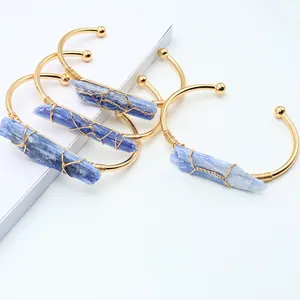 Detail eines handgefertigten vergoldeten Armreifs mit blauem Rohkristall und Drahtwicklung