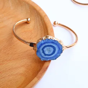 Detalle de brazalete abierto dorado con geoda de ágata azul redonda y puntas esféricas