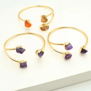 Detail van drie goudkleurige armbanden met natuurlijke amethist en rode agaat in ruwe stijl