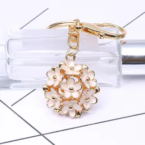 Détail d'un porte-clés boule de fleurs dorée avec émail blanc et fermoir mousqueton
