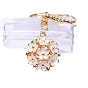 Porte-clés doré avec boule florale creuse et petites pâquerettes en émail blanc brillant