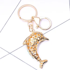 Porte-clés dauphin doré avec motif de cœur évidé et strass bleus sur fond blanc épuré