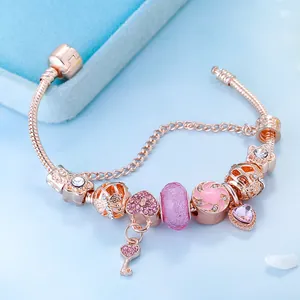 Roségoldenes Schlangenarmband mit rosa Herzanhängern und Kristallperlen auf blauem Grund