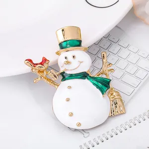 Broche bonhomme de neige en émail blanc avec bords dorés et écharpe verte sur bureau
