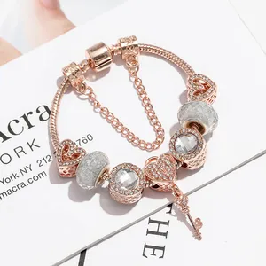 Bracciale in oro rosa con ciondoli a cuore e chiave e cristalli su sfondo minimalista