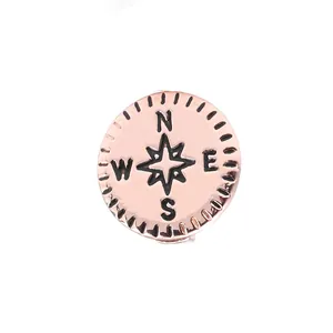 Vue macro d'un charm boussole en or rose avec rose des vents et gravure des directions