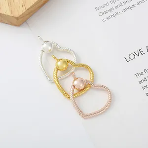 Trois pendentifs cœur en or, argent et or rose avec bords torsadés sur une carte blanche
