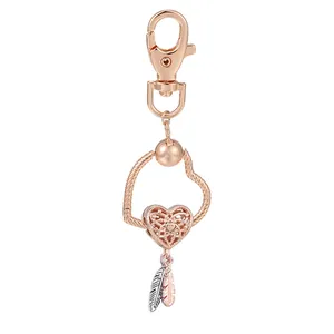 Porte-clés cœur or rose avec pendentifs ailes d'ange et plumes sur fond blanc neutre