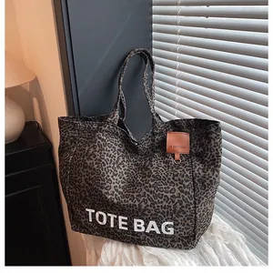 Close-up of leopard print canvas tote bag featuring brown leather logo label and metal ring