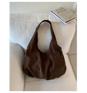 Dettaglio borsa hobo in pelle scamosciata marrone su divano bianco con tracolla