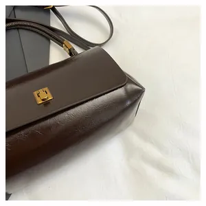 Dettaglio di borsa in pelle lucida marrone scuro con chiusura quadrata in metallo dorato