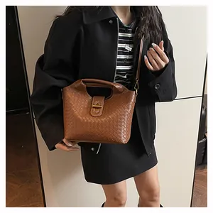 Dettaglio di una borsa intrecciata marrone con texture pregiata e fibbia dorata