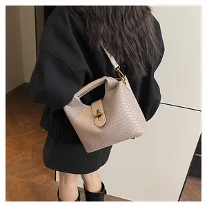 Dettaglio di una borsa beige intrecciata con chiusura dorata indossata da una modella
