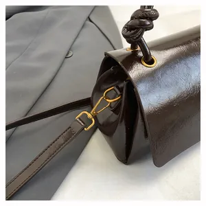 Dettaglio borsa in pelle lucida marrone scuro con manico a nodo e componenti metallici oro