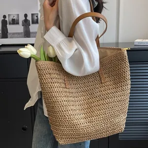 Detail of hand-woven straw tote bag with brown PU leather handles and metal zipper closure
