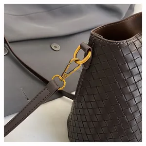 Dettaglio borsa a secchiello in pelle intrecciata marrone con ganci in metallo oro