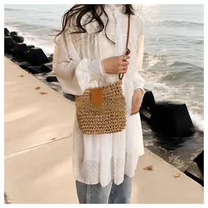Detail of hand-woven straw crossbody bag with leather strap against seaside background