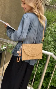 Detail of hand-woven crossbody bag featuring textured circular flap and decorative pompoms