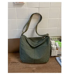 Dettaglio della borsa a tracolla in tela a scacchi verde scuro con tracolla regolabile su legno