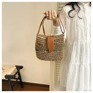 Detailed close-up of woven straw handbag featuring premium brown leather strap and metal buckle