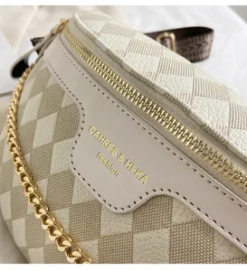 Detail shot of beige waist bag featuring litchi texture with gold zipper and chain strap