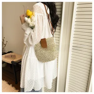 Detail of hand-woven straw crossbody bag with brown leather strap and snap closure