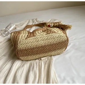 Dettaglio della borsa tote in paglia a righe con nappe decorative in legno e resina