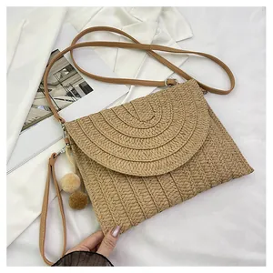Close-up of woven straw shoulder bag with plush pom-poms and leather strap details